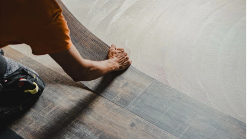 Construction worker installing luxury vinyl plank flooring using glue down method