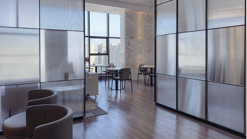A space with white marble desk with two comfortable gray chairs. A partition made of glass panels 
