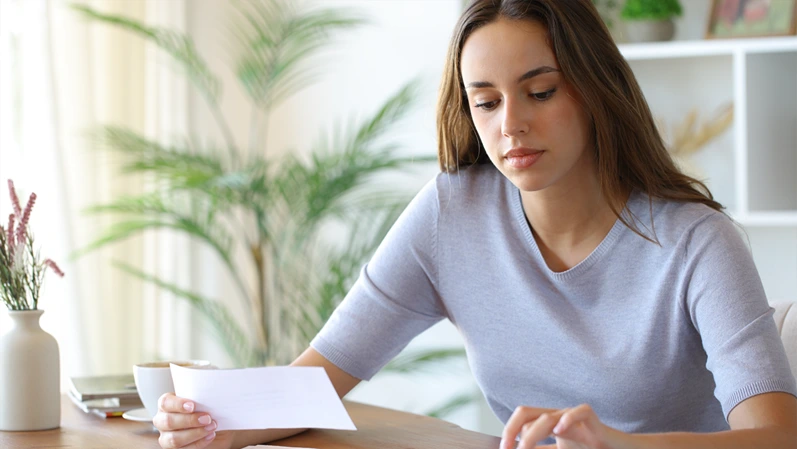 Woman using calculator holding bill on a wooden table in a room at home