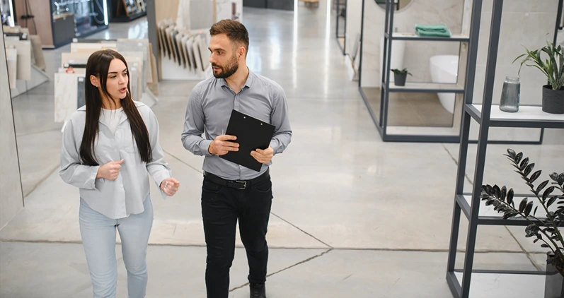 Sales assistant consulting a woman in a modern bathroom and tile showroom discussing renovation