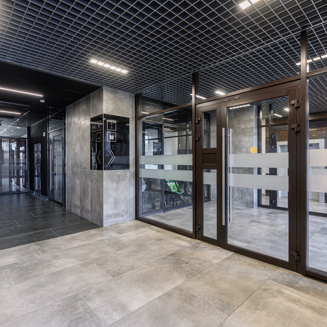Modern lobby featuring tile floors, glass doors, a grid ceiling with lights, and a security system