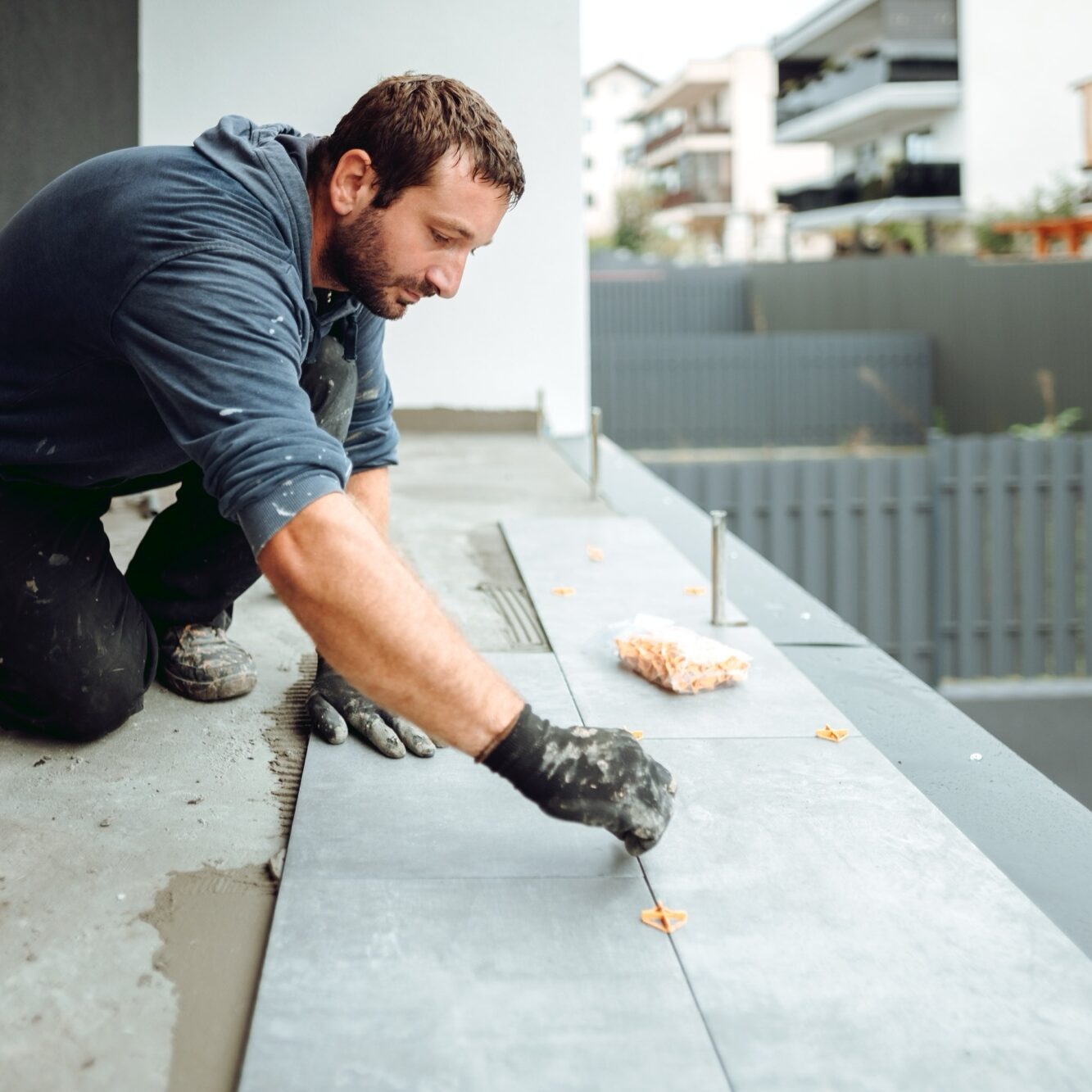 industrial worker, handyman installing big ceramic tiles on bathroom walls. Balcony area covered in ceramic tiles with strong adhesive